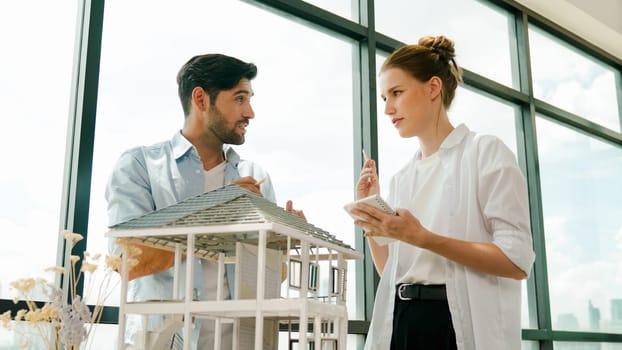 Skilled architect engineer team discussion about house model construction. Smart interior designer sharing, talking about building design while beautiful coworker taking a note. Design. Tracery