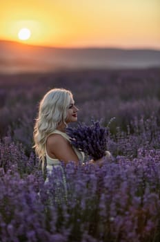 Blonde woman poses in lavender field at sunset. Happy woman in white dress holds lavender bouquet. Aromatherapy concept, lavender oil, photo session in lavender.