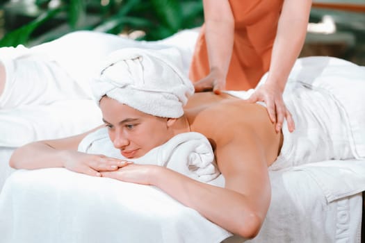 Beautiful young woman received a back massage on a spa bed from professional masseuse. Attractive female relaxes deeply by skilled hands of the massage therapist. Surrounded with nature. Tranquility.