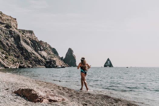 Woman beach vacation photo. A happy tourist in a blue bikini enjoying the scenic view of the sea and volcanic mountains while taking pictures to capture the memories of her travel adventure