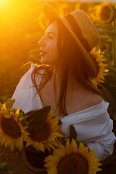 A girl in a hat on a beautiful field of sunflowers against the sky in the evening light of a summer sunset. Sunbeams through the flower field. Natural background