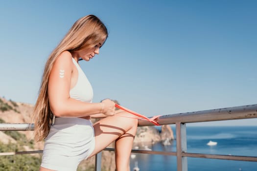 Young woman with black hair, fitness instructor in pink sports leggings and tops, doing pilates on yoga mat with magic pilates ring by the sea on the beach. Female fitness daily yoga concept