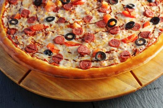 Pepperoni pizza adorned with black olives and red bell pepper slices, presented on a round wooden board