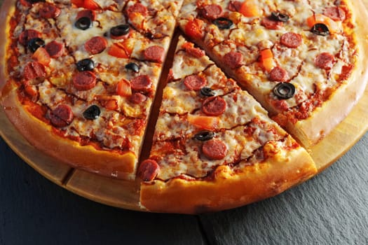 Pepperoni pizza adorned with black olives and red bell pepper slices, presented on a round wooden board