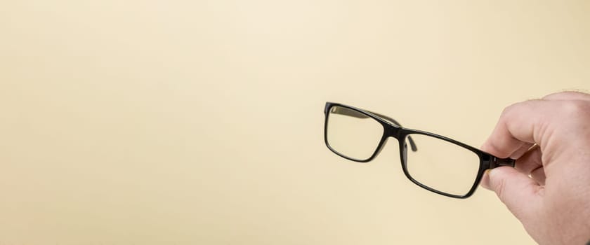 Hand holding black framed prescription glasses in front of yellow background