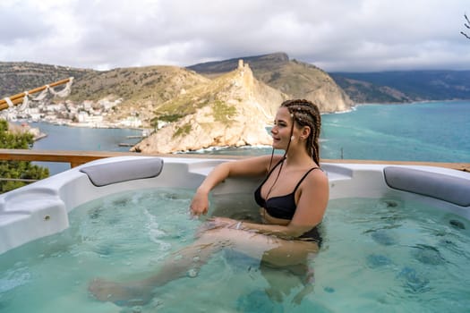 Take time for yourself. Outdoor swimsuit with mountain and sea views. A woman in a black swimsuit is relaxing in the hotel pool, admiring the view.