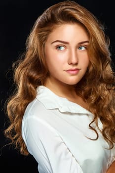 Portrait beautiful young brunette woman with wavy hair in white clothes, looks into the distance, isolated on dark background