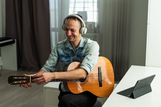 Man wearing headphones, sitting at desk with guitar, happy musician artist reading good comments in social networks. High quality photo
