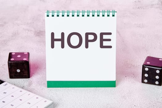 HOPE text on a white notepad sheet next to dice on an abstract background