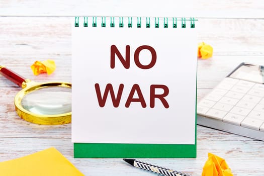 NO WAR text on the white sheet of the notebook is next to a magnifying glass, calculator, pencil, stickers