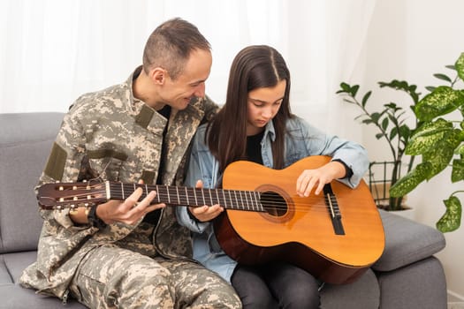 The veteran came back from army. A man in uniform with his daughter. The veteran is playing the guitar. High quality photo