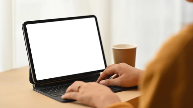 Side view of young creative woman working online on digital tablet in bright living room.