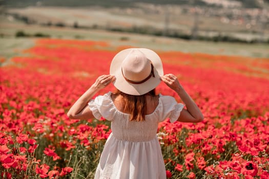 Field poppies woman. Happy woman in a white dress and hat stand through a blooming field of poppy raised her hands up. Field of blooming poppies