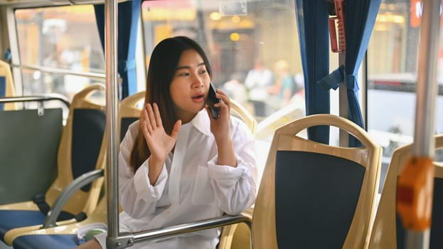 Young woman passenger sitting inside public bus and talking on mobile phone. City life and transportation concept.