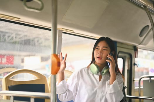 Young woman talking on mobile phone while traveling by bus. City life and transportation concept.