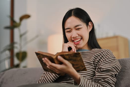 Happy young woman enjoying novel story, relaxing on couch at cozy home.