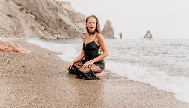 Woman travel sea. Young Happy woman in a long red dress posing on a beach near the sea on background of volcanic rocks, like in Iceland, sharing travel adventure journey