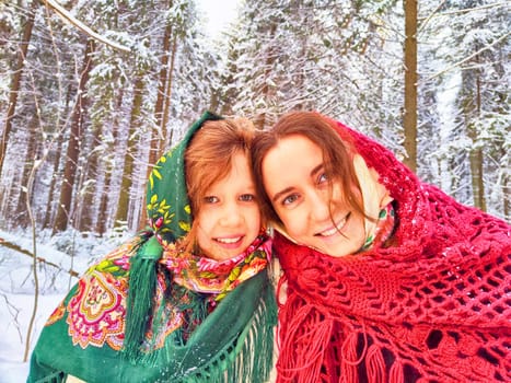 Portrait of happy family. Mother and daughter in shawls in winter forest. Ethnic clothes for carnival Maslenitsa