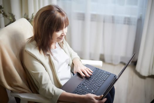 Elderly lady with a laptop in the room. A businesswoman is a leader, a manager is working. Grandma communicates with her grandchildren on the Internet