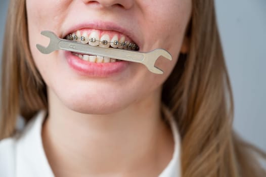 Close-up portrait of a woman with braces holding a wrench in her teeth