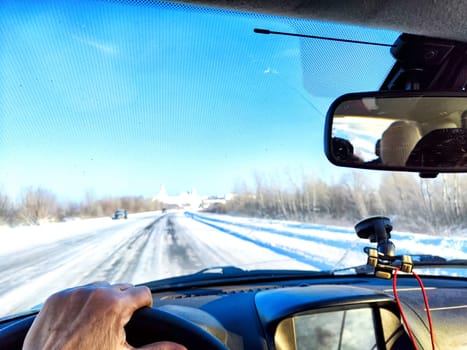 Hand of woman on the steering wheel in car and view through the windshield of a winter road with snow-covered trees