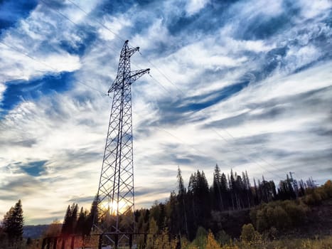 Power lines on a hill, hill or in the mountains against a blue sky with white clouds. Electric lines, towers, wires in nature landscape