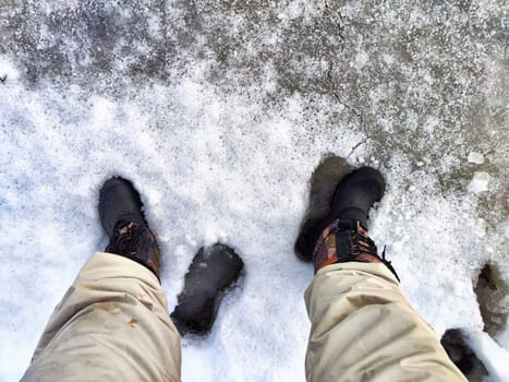 Feet of Hunter or fisherman in big warm boots on winter day on snow. Top view. Fisherman on the ice of a river, lake, reservoir on spring day with melting ice. Dangerous fishing in autumn