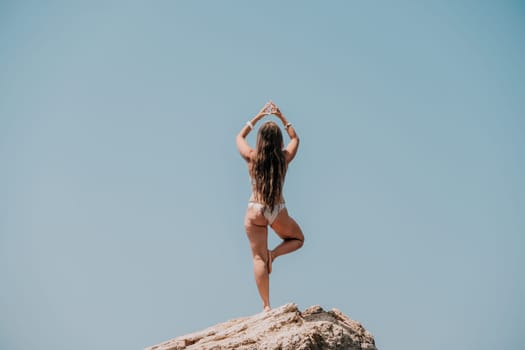 Woman meditating in yoga pose silhouette at the ocean, beach and rock mountains. Motivation and inspirational fit and exercising. Healthy lifestyle outdoors in nature, fitness concept.