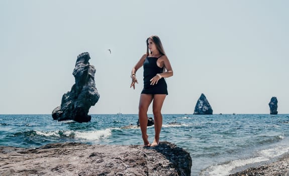 Woman travel sea. Young Happy woman in a long red dress posing on a beach near the sea on background of volcanic rocks, like in Iceland, sharing travel adventure journey