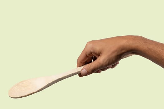 Black male hand holding a wooden cooking spoon isolated on light green background. High quality photo