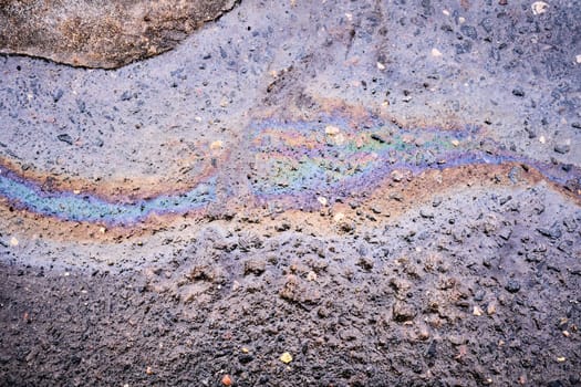 Fuel or oil spills on an asphalt road after melted snow as a texture or background