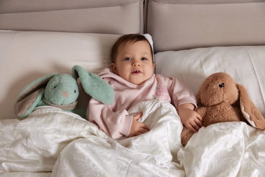 cute little child with fluffy toy bunny in white bed