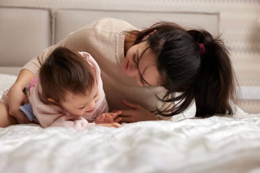 happy mother playing with her cute baby daughter on bed in bedroom. loving family having fun