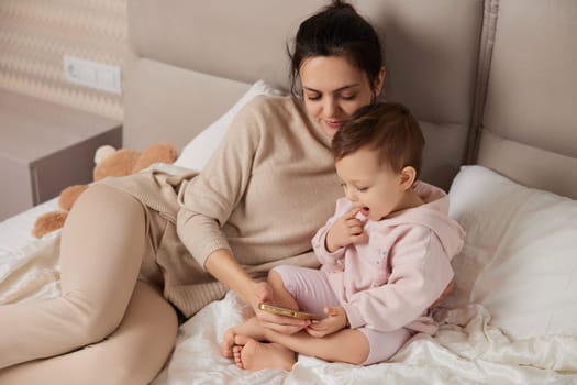 Mother and child playing online game on smartphone in bedroom at home