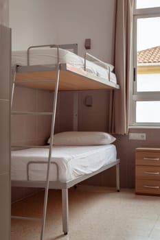 A clean and minimalistic hostel room with a bunk bed, white bedding, and a small wooden bedside table, ideal for budget travelers seeking affordable accommodation. Cheap hostels, save money