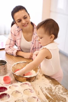 young mother and little baby girl preparing the dough in the kitchen, bake cookies. happy time together