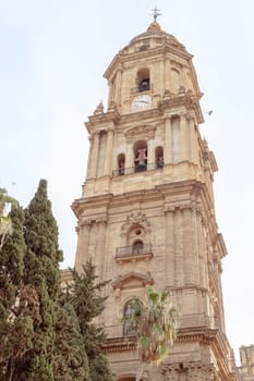 Malaga, Spain- 26-01-2024: Elegant tower of the Santa Iglesia Catedral Basilica de la Encarnacion, framed by greenery under a clear sky, perfect for cultural publications