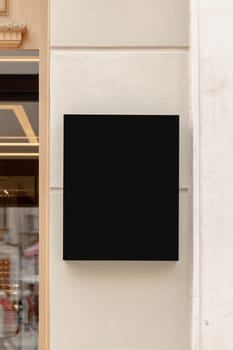 Wall-mounted black signboard on a textured wall, ideal for businesses to display their brand logo or promotional content. Black signage mockup