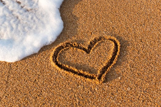 Heart drawn in the sand on the beach at sunset. Heart shape. Heart symbol. Love. Sea foam.