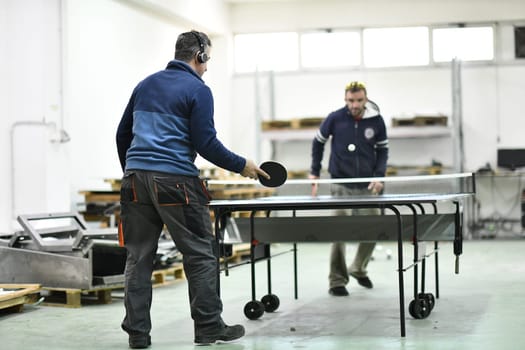 group of industry workers playing ping pong or table tennis game and relaxing in their free time at modern creative metal industry production factory