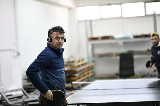 group of industry workers playing ping pong or table tennis game and relaxing in their free time at modern creative metal industry production factory