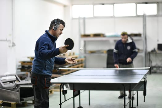 group of industry workers playing ping pong or table tennis game and relaxing in their free time at modern creative metal industry production factory