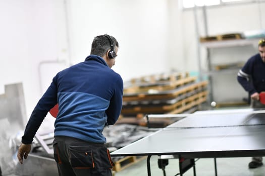 group of industry workers playing ping pong or table tennis game and relaxing in their free time at modern creative metal industry production factory