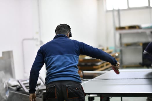 group of industry workers playing ping pong or table tennis game and relaxing in their free time at modern creative metal industry production factory