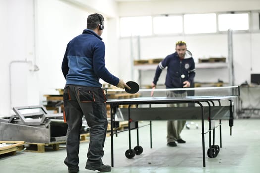 group of industry workers playing ping pong or table tennis game and relaxing in their free time at modern creative metal industry production factory