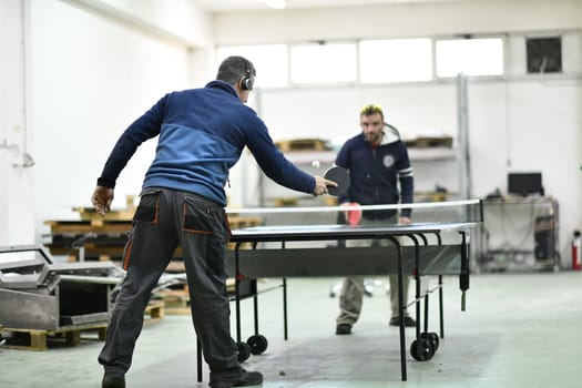 group of industry workers playing ping pong or table tennis game and relaxing in their free time at modern creative metal industry production factory