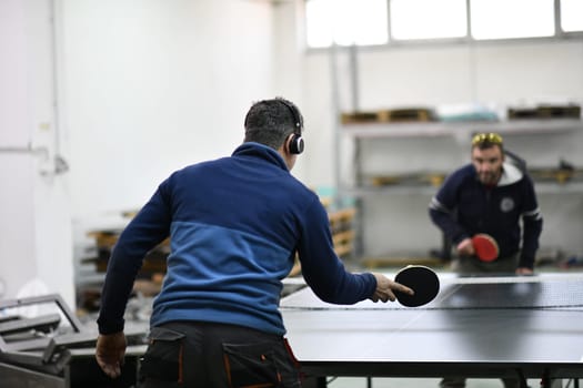 group of industry workers playing ping pong or table tennis game and relaxing in their free time at modern creative metal industry production factory