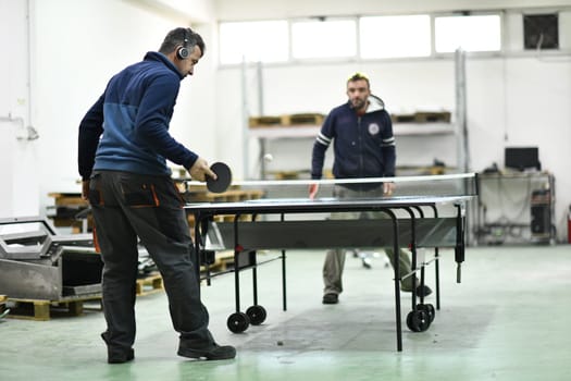 group of industry workers playing ping pong or table tennis game and relaxing in their free time at modern creative metal industry production factory