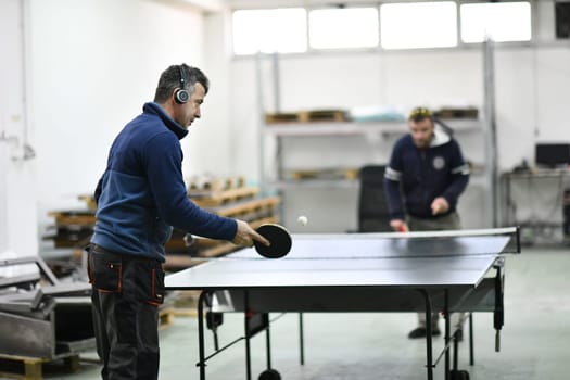 group of industry workers playing ping pong or table tennis game and relaxing in their free time at modern creative metal industry production factory