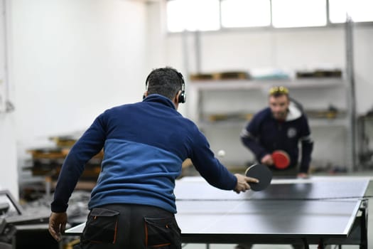 group of industry workers playing ping pong or table tennis game and relaxing in their free time at modern creative metal industry production factory